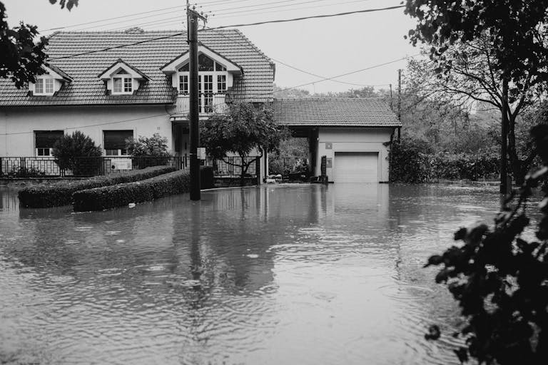 A flooded suburban house surrounded by high water, depicting severe weather impact.